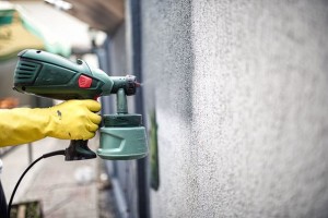 Worker painting wall with grey paint using a professional spray gun. Man painting wall using protective gloves